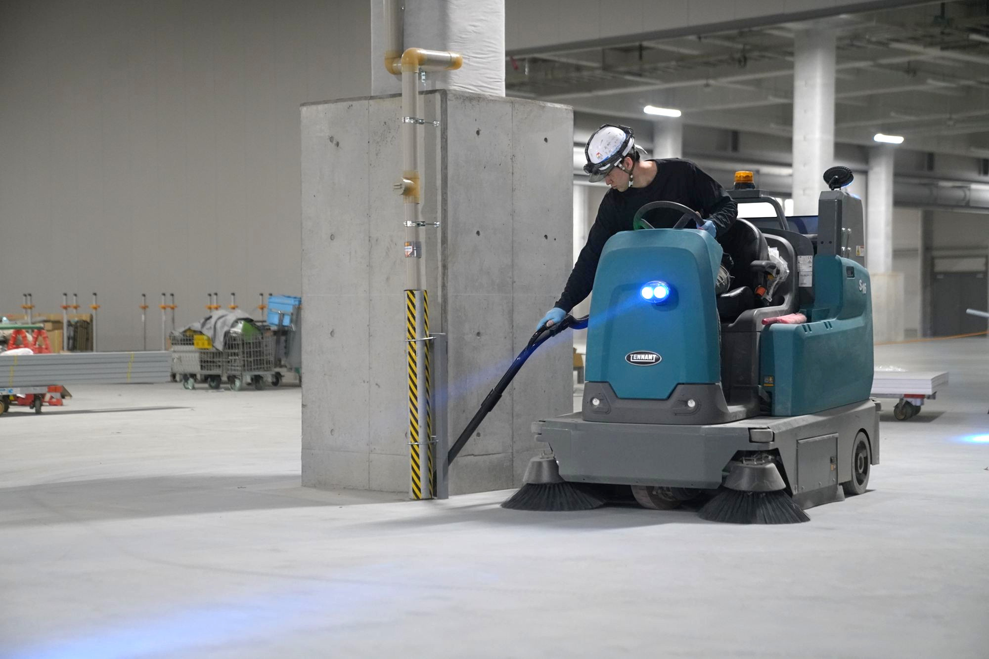 乗用式清掃機で物流倉庫の柱まわりを清掃する作業員